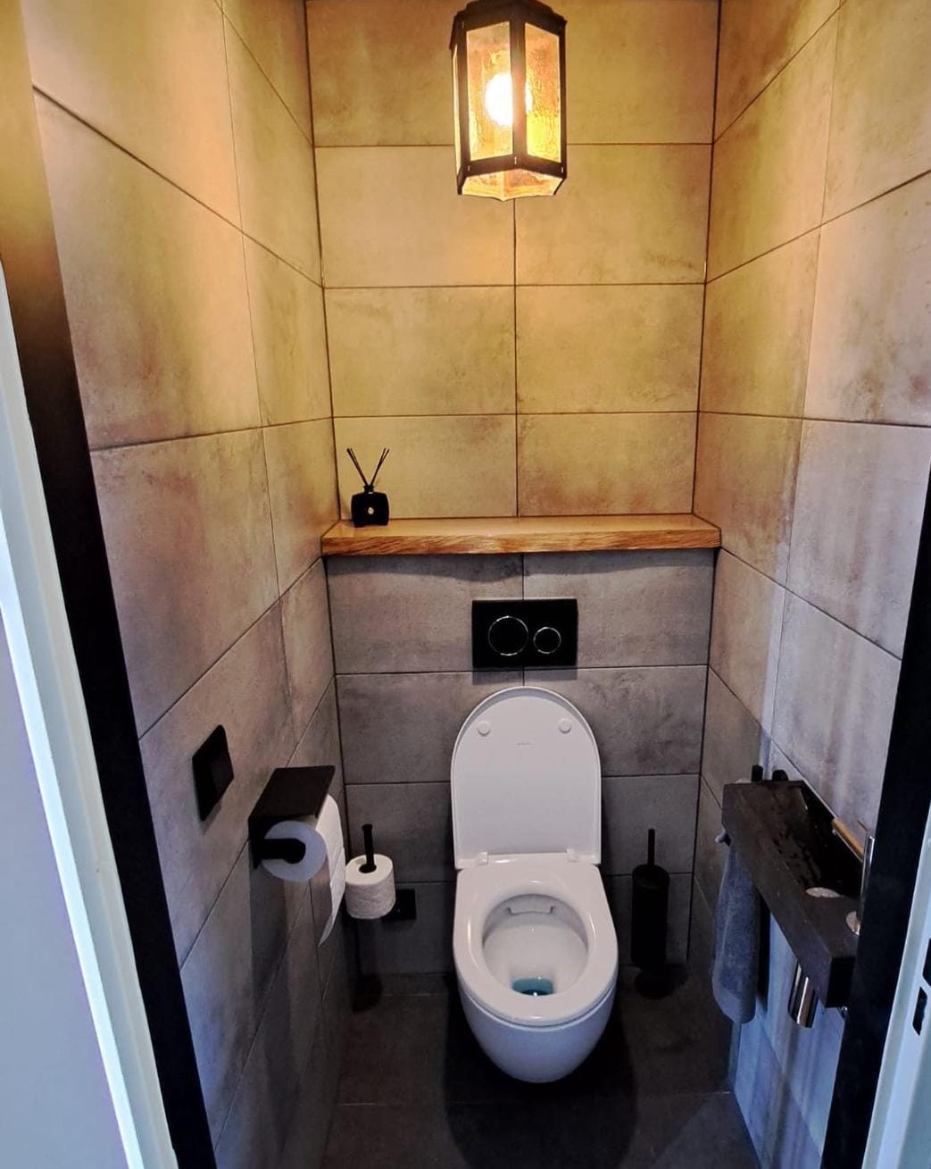 Toilet met betonlook tegels en een houten plank